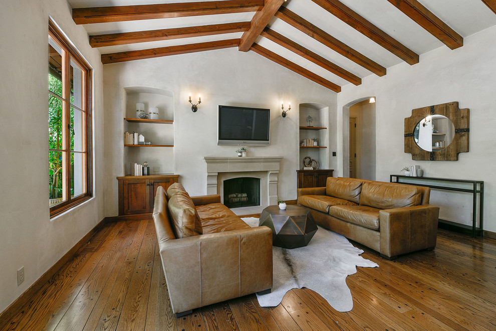 Diseño de sala de estar mediterránea con paredes blancas, suelo de madera en tonos medios, todas las chimeneas, marco de chimenea de piedra, televisor colgado en la pared y suelo marrón