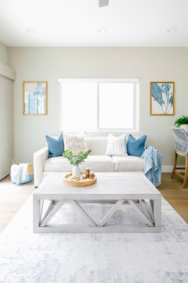 Imagen de sala de estar cerrada costera de tamaño medio con paredes grises, suelo de madera clara y televisor colgado en la pared
