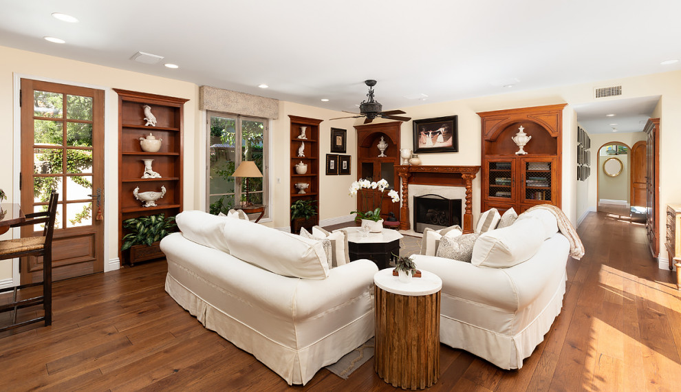 Cette image montre une très grande salle de séjour ouverte avec un bar de salon, un mur beige, un sol en bois brun, une cheminée standard, un manteau de cheminée en bois et un sol marron.