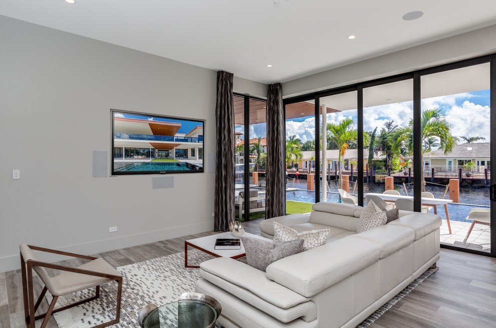 Großes, Offenes Modernes Wohnzimmer ohne Kamin mit weißer Wandfarbe, Kaminumrandung aus Metall, hellem Holzboden, TV-Wand und grauem Boden in Miami