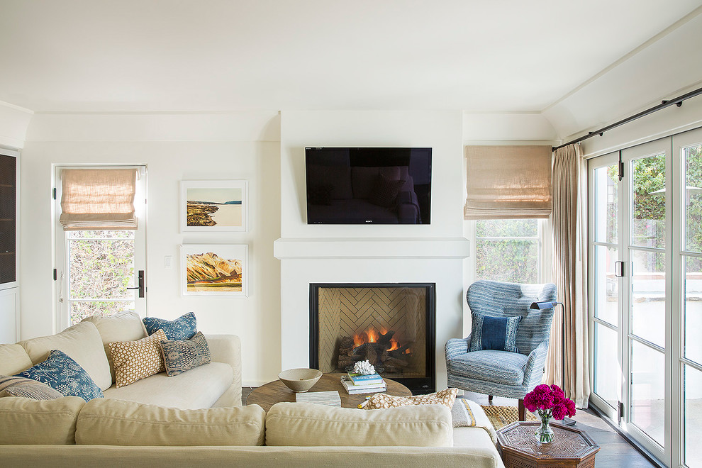 На фото: гостиная комната в средиземноморском стиле с белыми стенами, темным паркетным полом, стандартным камином и телевизором на стене с