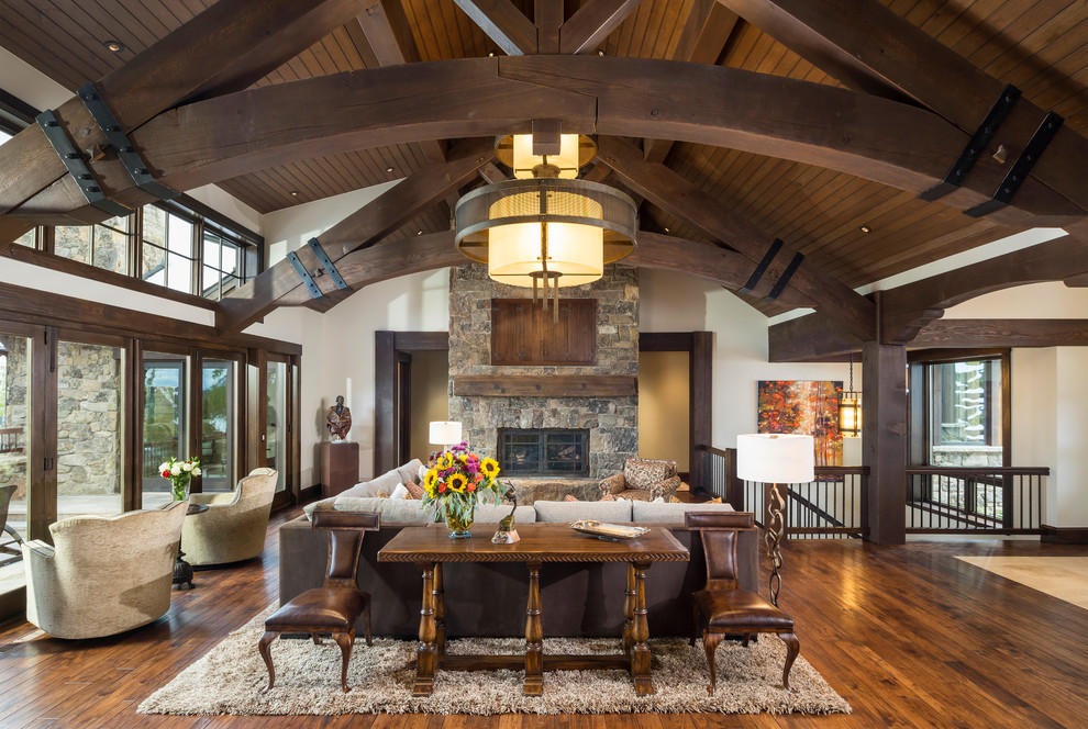 This is an example of a large rustic open plan games room in Salt Lake City with white walls, medium hardwood flooring, a standard fireplace, a stone fireplace surround, brown floors and a concealed tv.