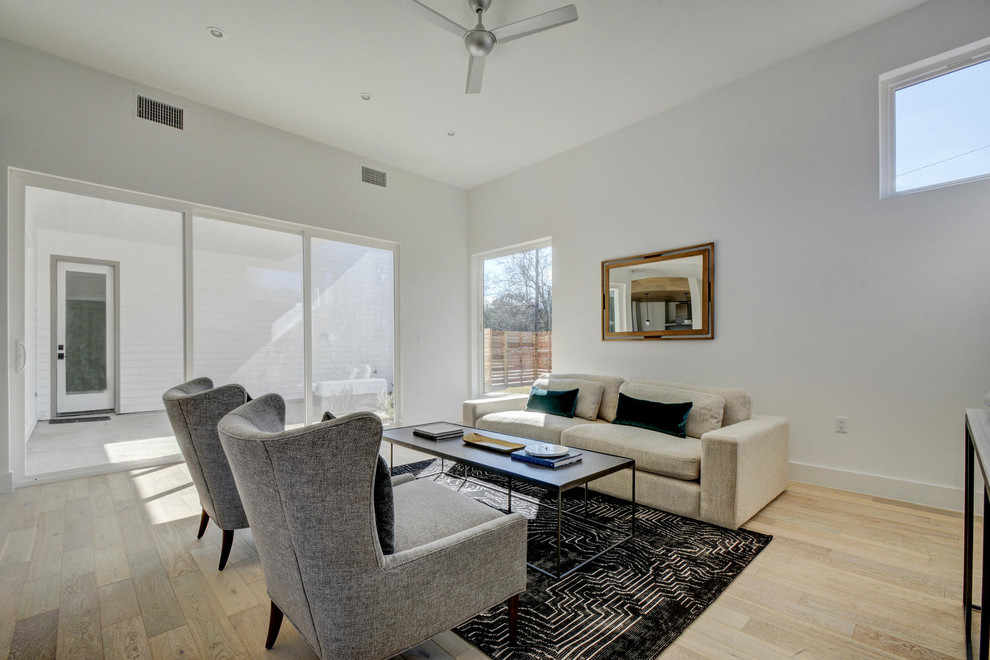 Imagen de sala de estar abierta minimalista grande con paredes blancas, suelo de madera clara y televisor independiente