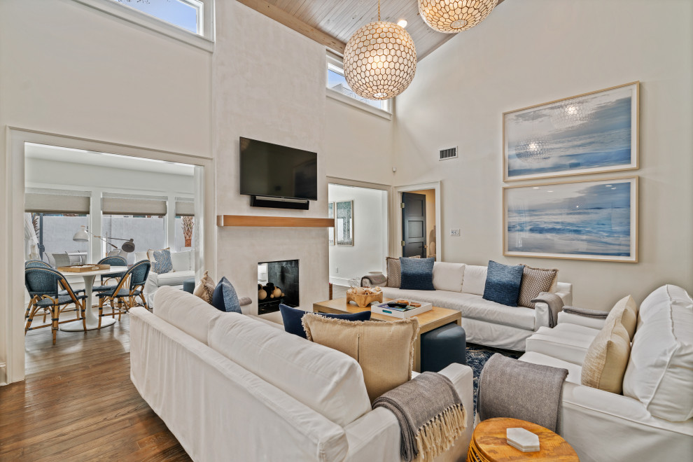 Ejemplo de sala de estar abierta marinera de tamaño medio con paredes blancas, suelo de madera en tonos medios, chimenea de doble cara, marco de chimenea de yeso y suelo gris