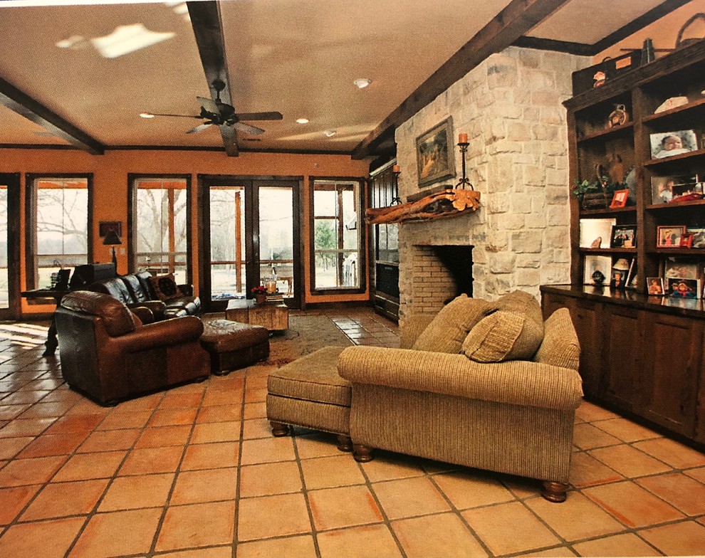 Modelo de sala de estar abierta rural grande con parades naranjas, suelo de baldosas de terracota, todas las chimeneas, marco de chimenea de piedra, televisor retractable y suelo naranja