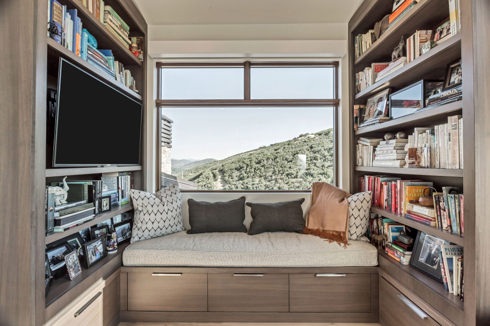 Diseño de sala de estar con biblioteca cerrada contemporánea sin chimenea con paredes beige, suelo de madera en tonos medios, televisor colgado en la pared y suelo marrón