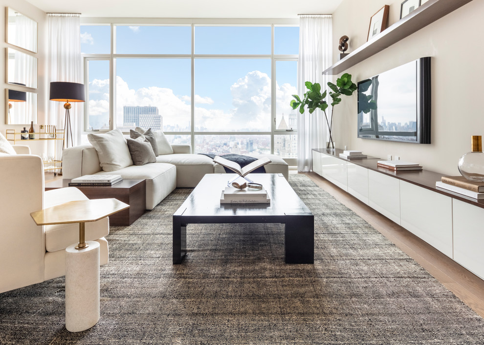 Offenes Modernes Wohnzimmer ohne Kamin mit Hausbar, beiger Wandfarbe, hellem Holzboden und TV-Wand in New York