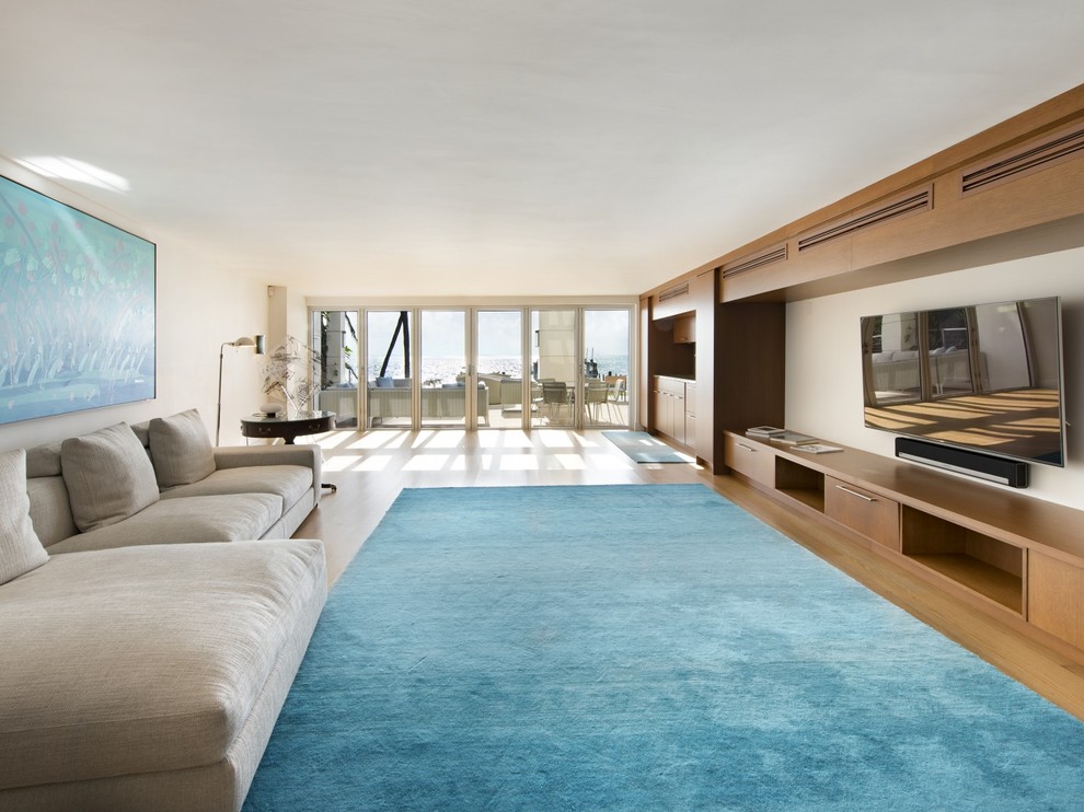 Стильный дизайн: открытая гостиная комната в стиле модернизм с белыми стенами, светлым паркетным полом и телевизором на стене - последний тренд