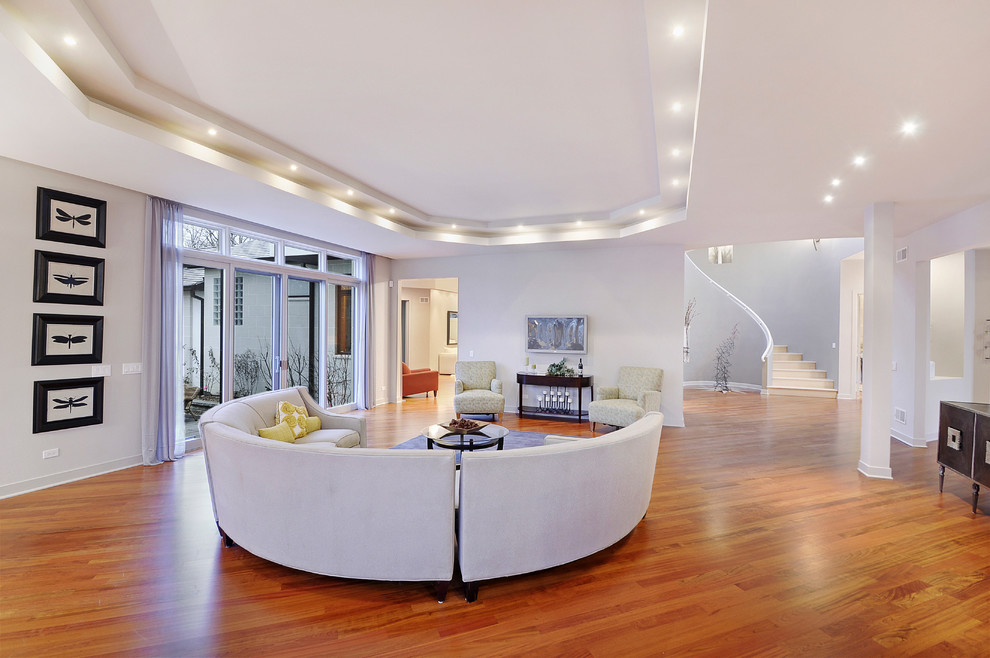 Ejemplo de sala de estar abierta contemporánea grande sin chimenea con suelo de madera en tonos medios, televisor colgado en la pared, paredes grises y suelo marrón
