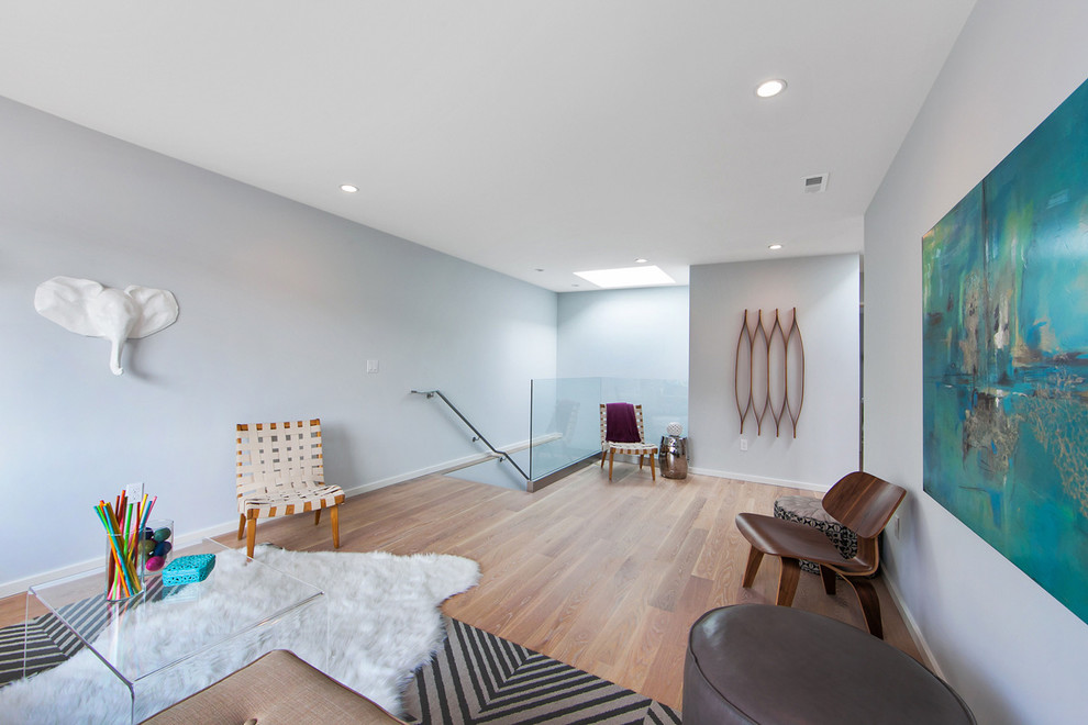 Ejemplo de sala de estar con biblioteca abierta actual de tamaño medio sin chimenea con paredes azules, suelo de madera en tonos medios y pared multimedia