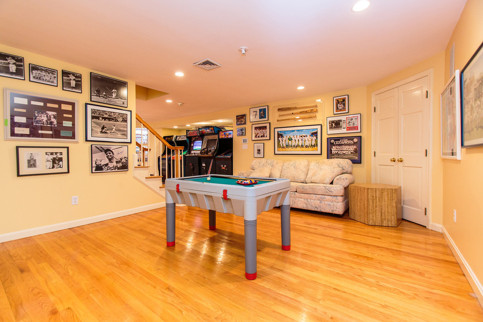 Modelo de sala de juegos en casa abierta tradicional grande con paredes blancas, suelo de madera en tonos medios y pared multimedia