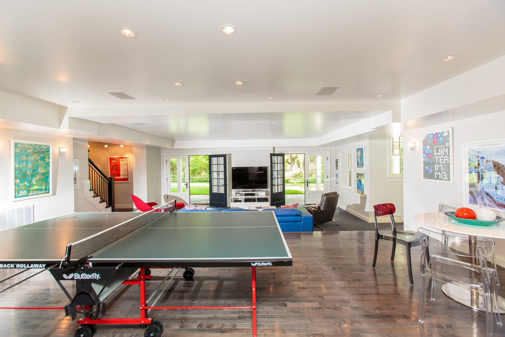 Imagen de sala de juegos en casa abierta tradicional grande con paredes blancas, suelo de madera en tonos medios y televisor independiente