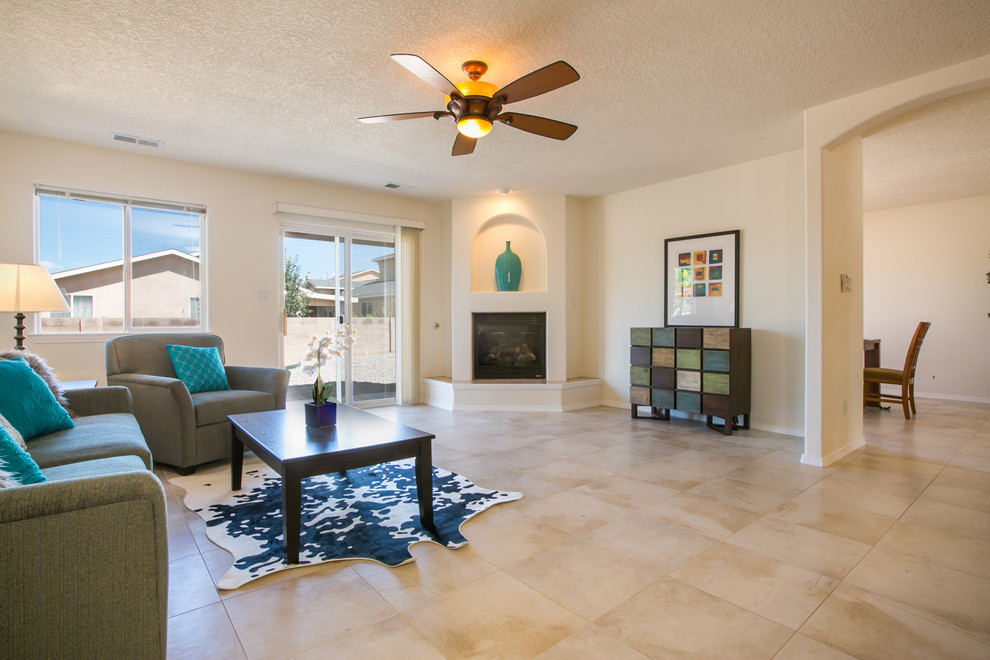 This is an example of a medium sized traditional open plan games room in Albuquerque with white walls, travertine flooring, a corner fireplace, a plastered fireplace surround and a wall mounted tv.