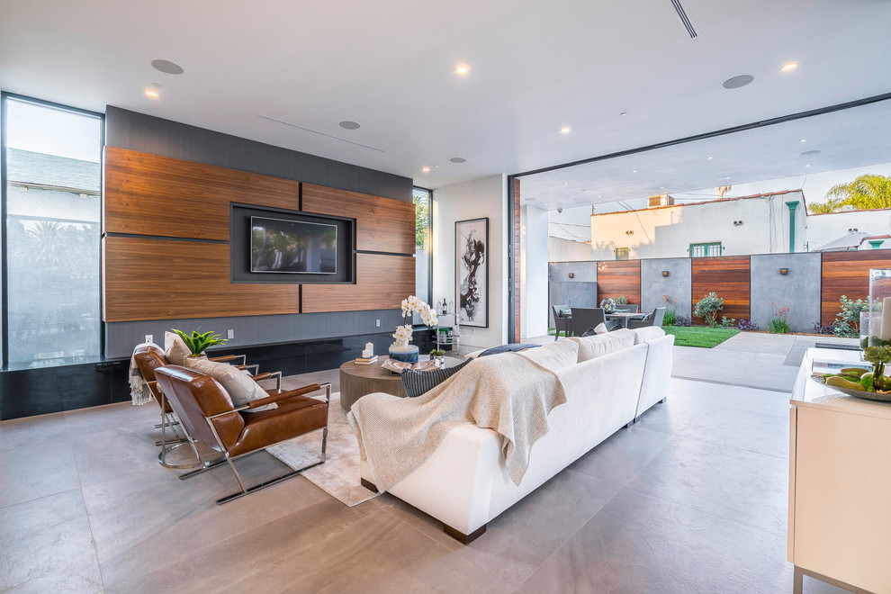 Diseño de sala de estar abierta actual extra grande sin chimenea con paredes beige, suelo de cemento, televisor colgado en la pared y suelo gris