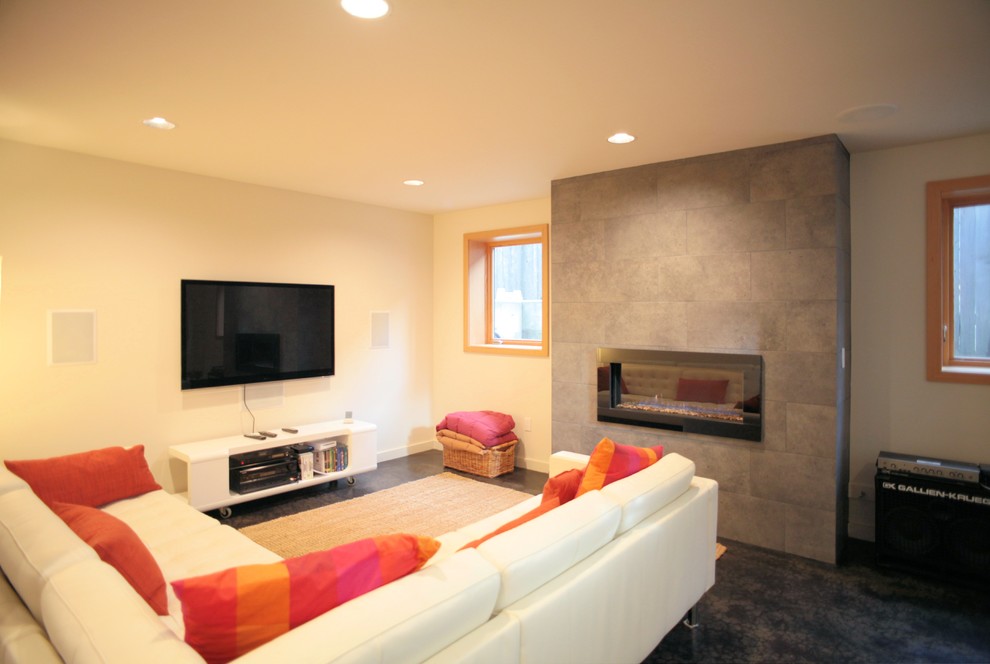 Ejemplo de sala de estar abierta moderna grande con paredes beige, suelo de cemento, chimenea lineal, marco de chimenea de baldosas y/o azulejos, televisor colgado en la pared y suelo negro