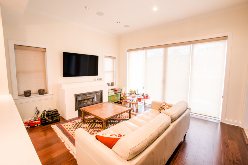 На фото: изолированная гостиная комната среднего размера в стиле неоклассика (современная классика) с белыми стенами, темным паркетным полом, стандартным камином, фасадом камина из штукатурки, телевизором на стене и коричневым полом