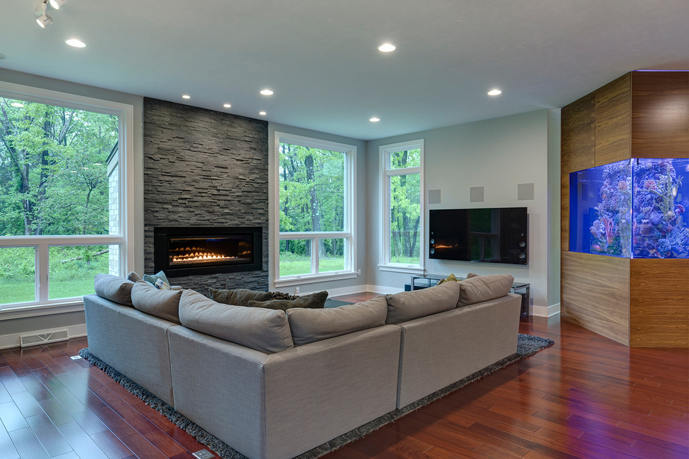 Example of a large trendy open concept medium tone wood floor family room design in Other with gray walls, a standard fireplace, a stone fireplace and a wall-mounted tv