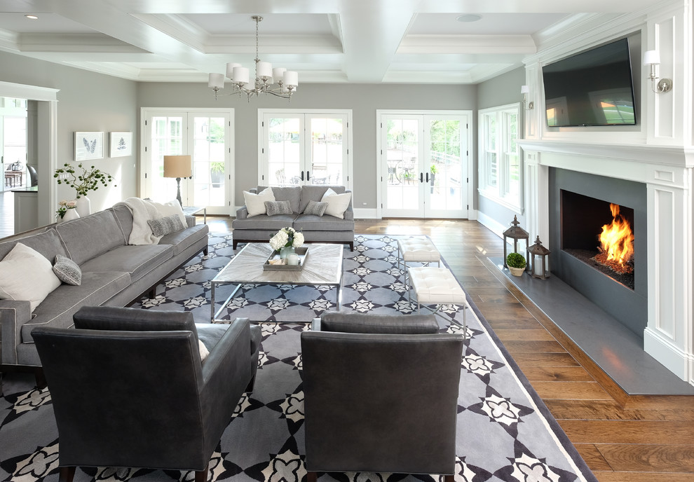 Imagen de sala de estar abierta tradicional renovada grande con paredes grises, suelo de madera en tonos medios, todas las chimeneas, marco de chimenea de piedra y televisor colgado en la pared