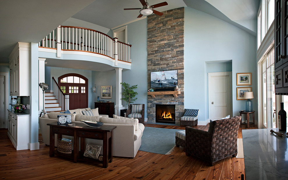 Example of a large beach style enclosed medium tone wood floor and brown floor family room design in Boston with blue walls, a standard fireplace, a stone fireplace and a wall-mounted tv