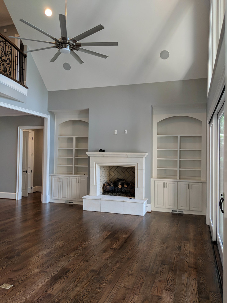 Foto de sala de estar abierta tradicional grande con paredes grises, suelo de madera en tonos medios, todas las chimeneas y televisor colgado en la pared