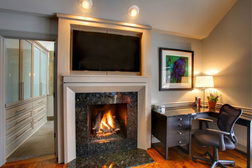 Exemple d'une salle de séjour chic de taille moyenne et ouverte avec un mur gris, un sol en bois brun, une cheminée standard, un manteau de cheminée en pierre, un téléviseur encastré et un sol marron.