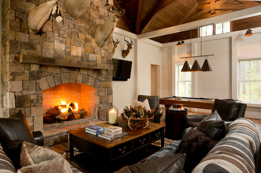 This is an example of a rustic games room in Atlanta with white walls, medium hardwood flooring, a standard fireplace, a stone fireplace surround and a wall mounted tv.