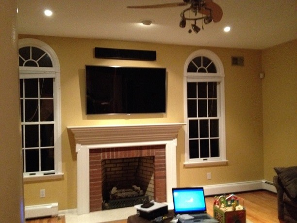 This is an example of a medium sized classic open plan games room in New York with yellow walls, a standard fireplace, a brick fireplace surround and a wall mounted tv.