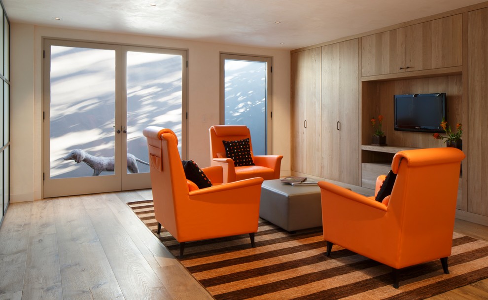 Стильный дизайн: гостиная комната в современном стиле с бежевыми стенами, паркетным полом среднего тона и телевизором на стене - последний тренд