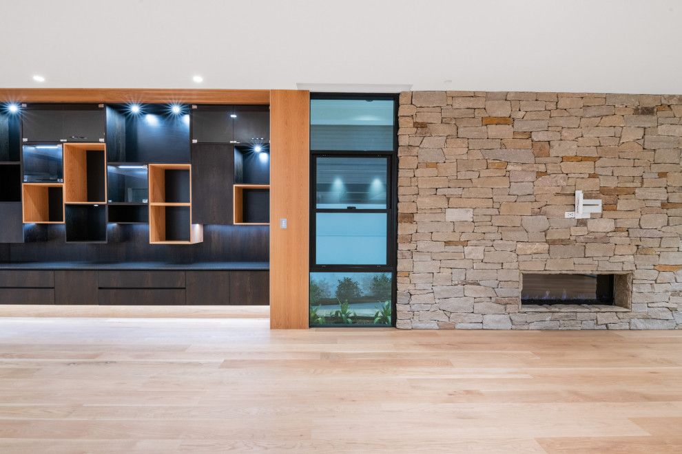 Diseño de sala de estar abierta moderna de tamaño medio con paredes blancas, suelo de madera en tonos medios, piedra de revestimiento y televisor colgado en la pared