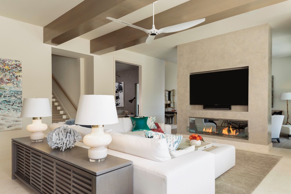 Modelo de sala de estar abierta tradicional renovada grande con paredes blancas, chimenea de doble cara, marco de chimenea de yeso y televisor colgado en la pared