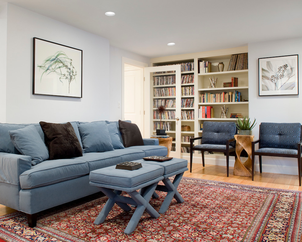 Modelo de sala de estar con biblioteca cerrada tradicional renovada con paredes blancas y suelo de madera en tonos medios
