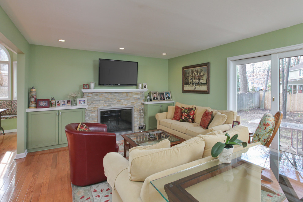 Foto de sala de estar abierta tradicional de tamaño medio con paredes verdes, suelo de madera clara, todas las chimeneas, marco de chimenea de piedra y televisor colgado en la pared