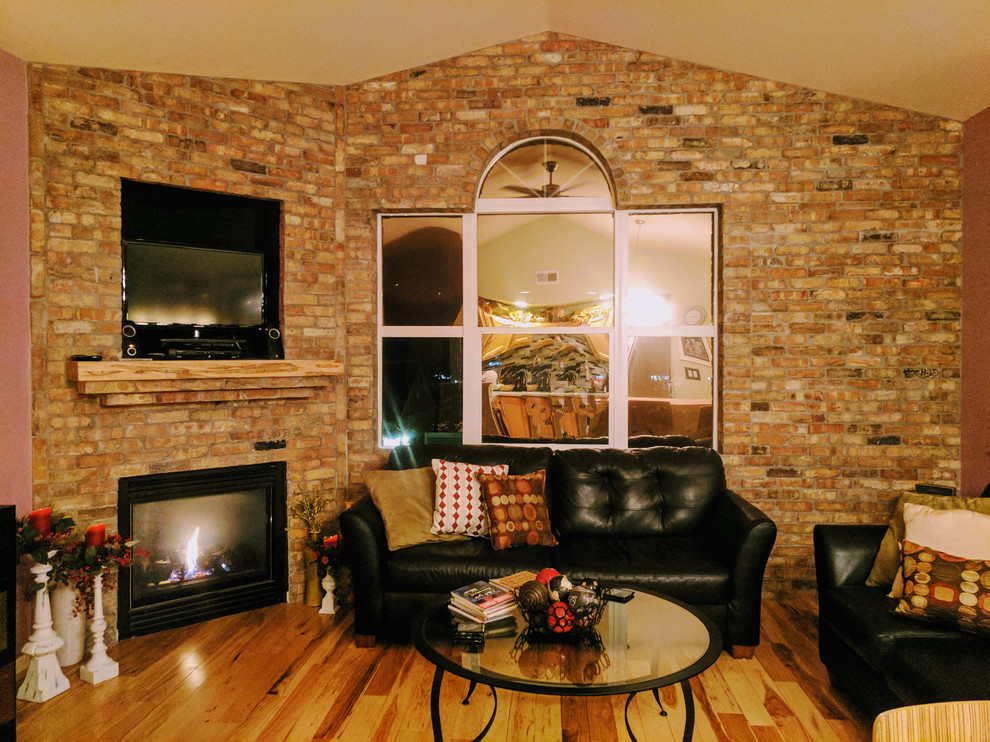 This is an example of a medium sized industrial mezzanine games room in Denver with light hardwood flooring, a corner fireplace and a brick fireplace surround.