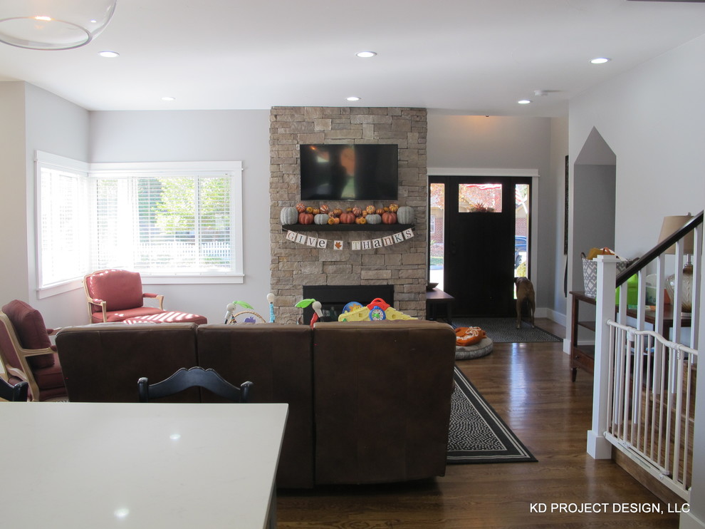 На фото: большая открытая гостиная комната в стиле неоклассика (современная классика) с серыми стенами, паркетным полом среднего тона, стандартным камином, фасадом камина из камня и телевизором на стене
