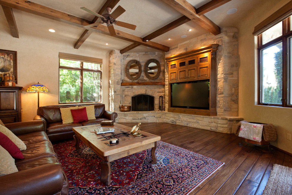 Ejemplo de sala de estar tradicional renovada de tamaño medio con chimenea de esquina, paredes beige, suelo de madera oscura, marco de chimenea de piedra y pared multimedia