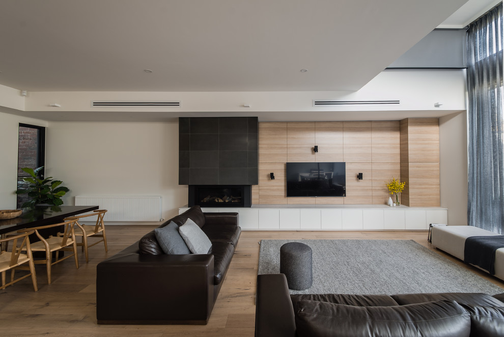 Modelo de sala de estar abierta moderna de tamaño medio con suelo de madera en tonos medios, marco de chimenea de piedra y chimenea lineal