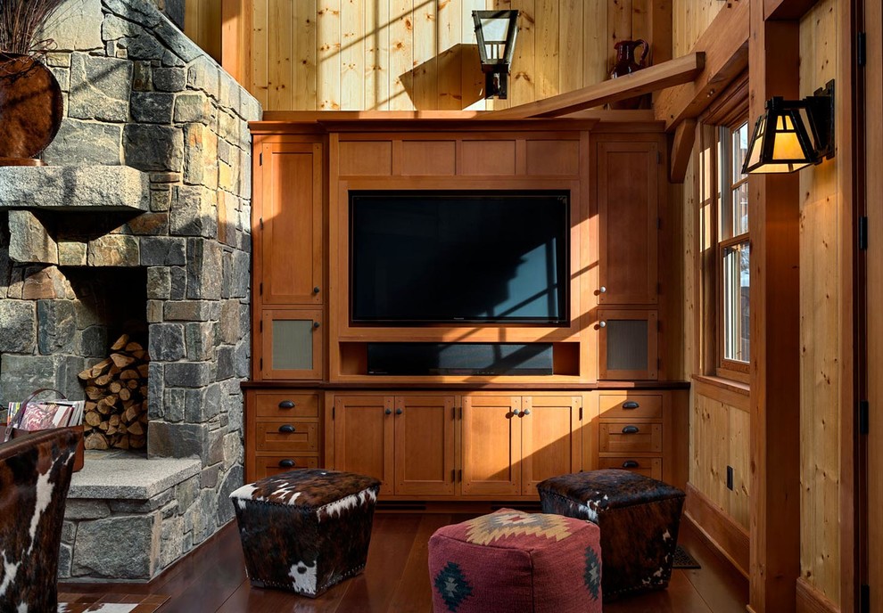 На фото: большая открытая комната для игр в стиле рустика с коричневыми стенами, темным паркетным полом, стандартным камином, фасадом камина из камня и мультимедийным центром с