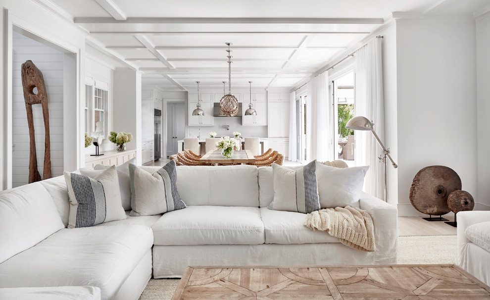 Diseño de sala de estar abierta actual grande con paredes blancas, suelo de madera clara y televisor colgado en la pared