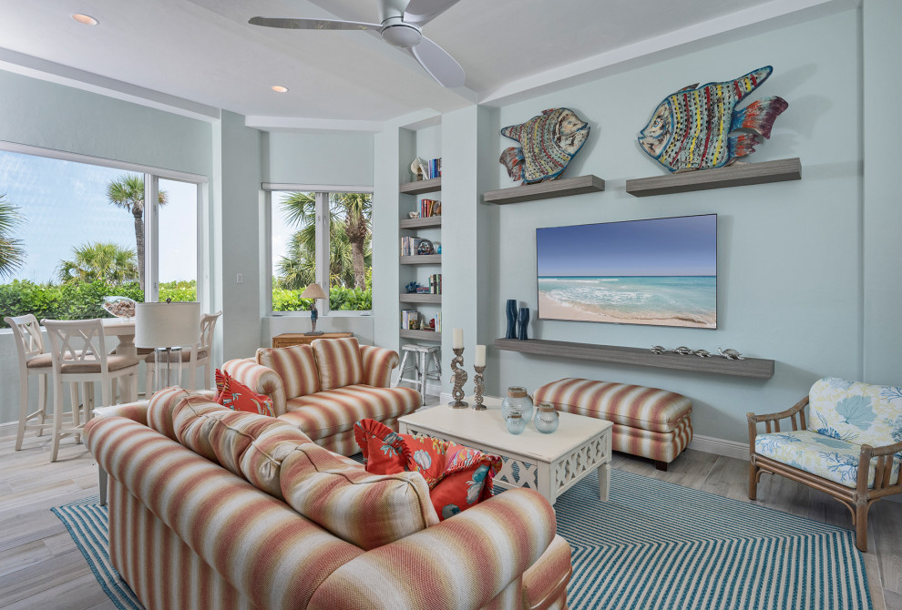 Modelo de sala de estar abierta marinera grande con paredes azules, suelo de baldosas de porcelana, televisor colgado en la pared y suelo beige