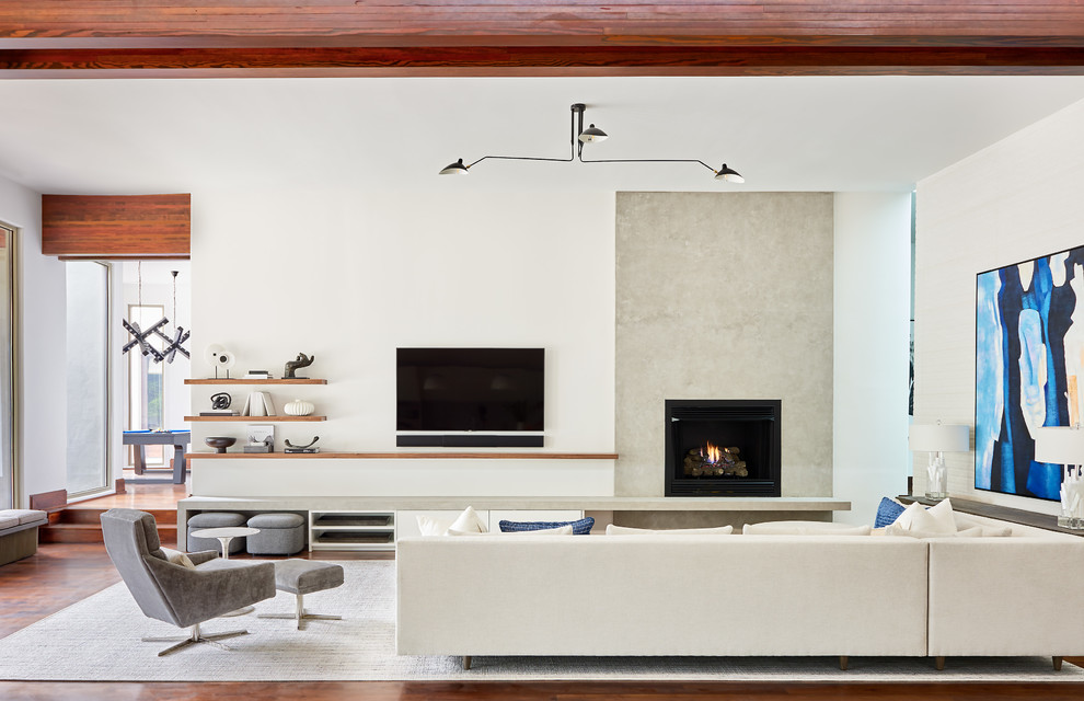 Пример оригинального дизайна: большая изолированная гостиная комната в современном стиле с белыми стенами, темным паркетным полом, стандартным камином, телевизором на стене, фасадом камина из бетона, коричневым полом и ковром на полу