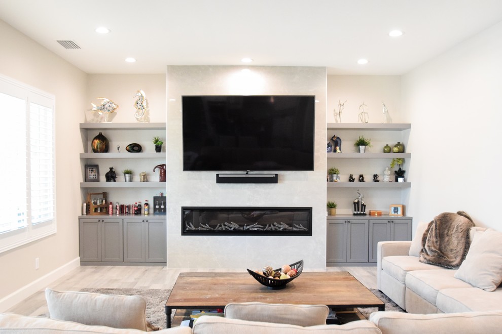 Cette image montre une grande salle de séjour minimaliste ouverte avec un mur gris, un sol en carrelage de porcelaine, cheminée suspendue, un manteau de cheminée en carrelage, un téléviseur encastré et un sol gris.