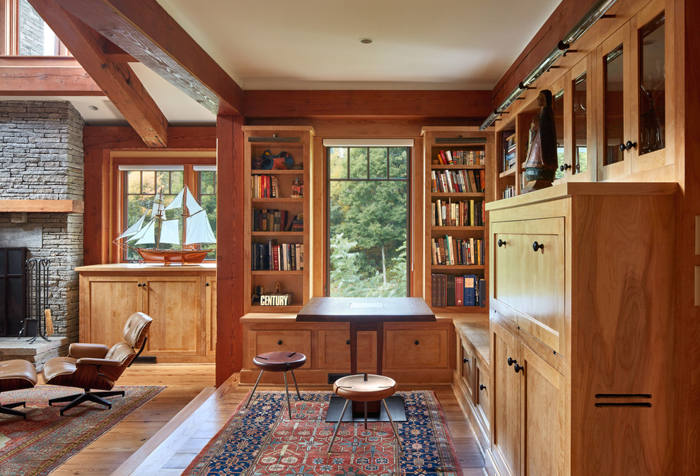 Cette image montre une salle de séjour chalet avec une bibliothèque ou un coin lecture, un sol en bois brun, une cheminée standard, un manteau de cheminée en pierre et un sol marron.