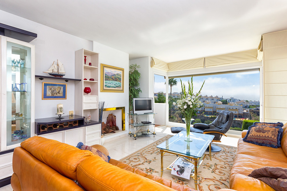 Modelo de sala de estar cerrada mediterránea grande con paredes blancas, suelo de travertino, todas las chimeneas, marco de chimenea de metal y televisor independiente