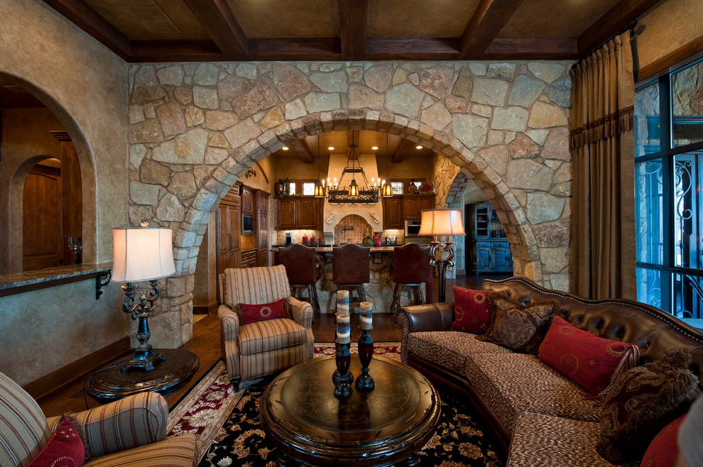 Ejemplo de sala de estar abierta mediterránea extra grande con paredes beige, suelo de madera en tonos medios, todas las chimeneas y marco de chimenea de piedra