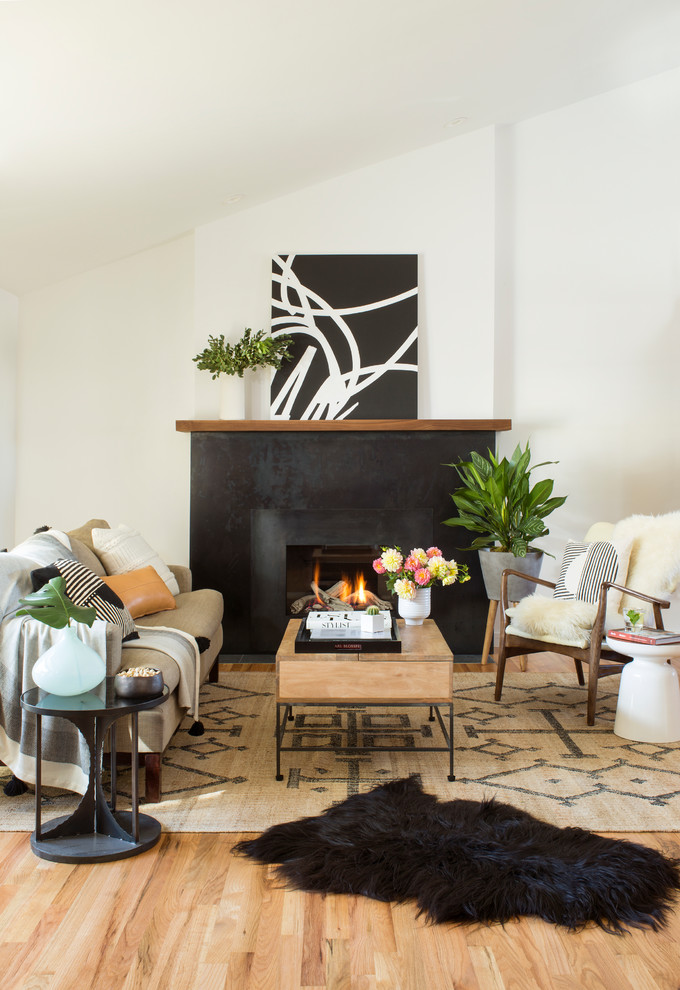 Imagen de sala de estar contemporánea con paredes blancas, suelo de madera clara, todas las chimeneas, marco de chimenea de metal y alfombra