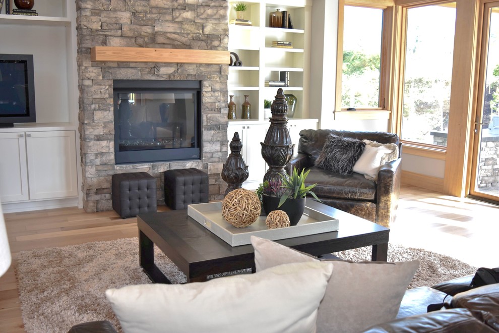 Diseño de sala de estar abierta de estilo americano grande con suelo de madera clara, todas las chimeneas, marco de chimenea de piedra, pared multimedia y paredes grises