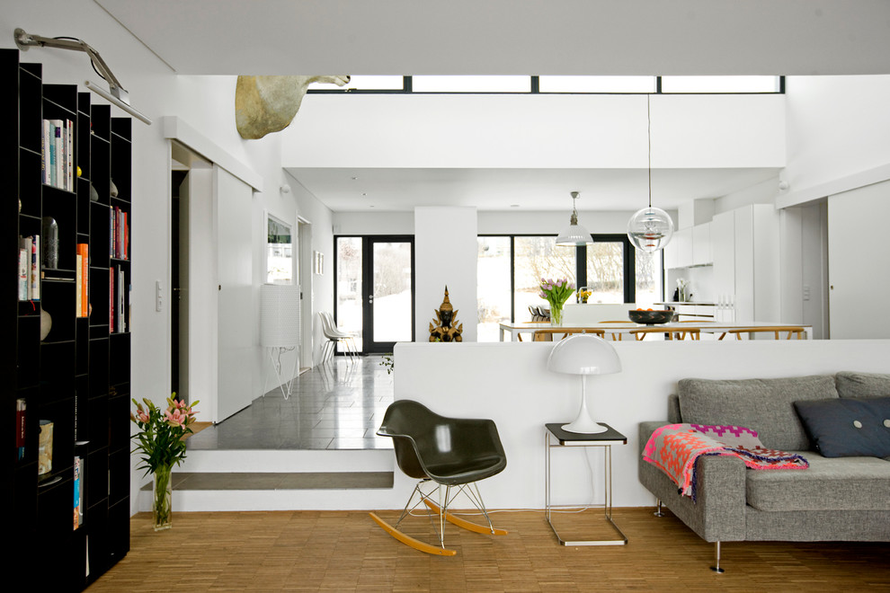 Modelo de sala de estar actual grande sin chimenea con paredes blancas, suelo de madera en tonos medios y suelo marrón