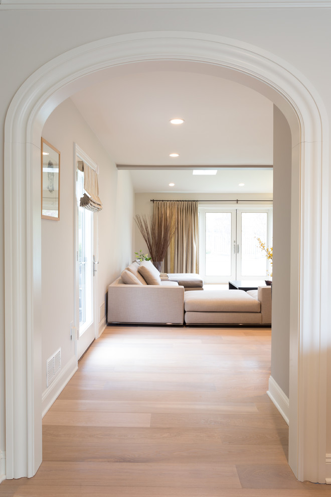 Diseño de sala de estar abierta retro grande con paredes beige, suelo de madera clara, chimenea de doble cara, marco de chimenea de piedra y pared multimedia