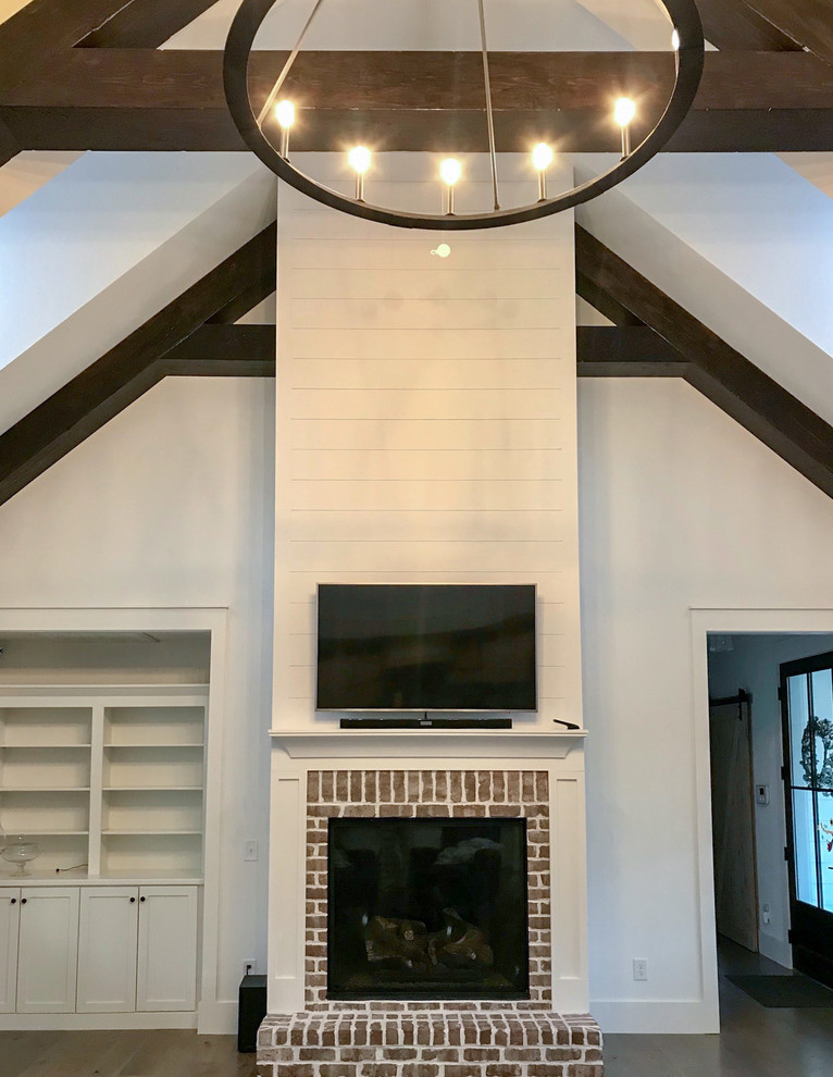 Offenes Landhausstil Wohnzimmer mit weißer Wandfarbe, Kamin, Kaminumrandung aus Backstein und TV-Wand in Sonstige