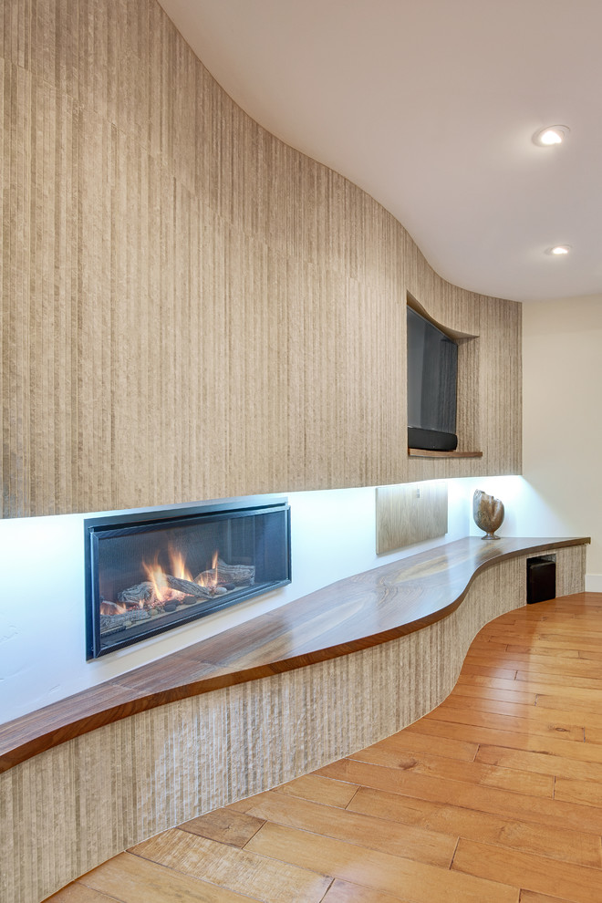 Cette image montre une salle de séjour craftsman de taille moyenne et ouverte avec un mur gris, un sol en bois brun, une cheminée standard, un manteau de cheminée en carrelage et un téléviseur encastré.